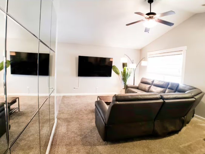 Living room with black leather sectional, wall-mounted TV and vaulted ceiling