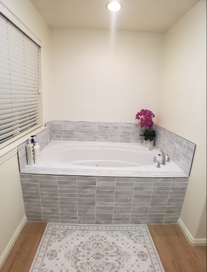 Jetted soaking tub with gray tile surround, pink orchid accent and wood flooring
