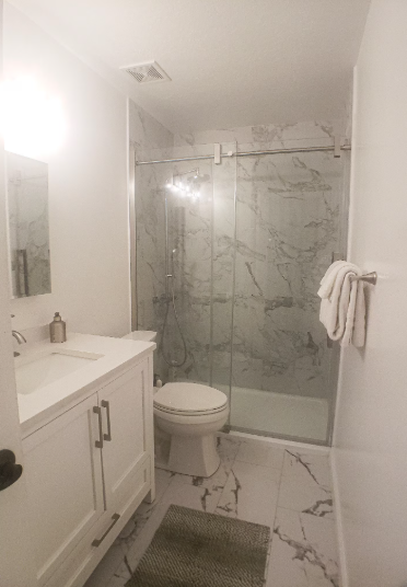 Remodeled bathroom with marble tile floors, glass slider shower enclosure, white vanity and white towels