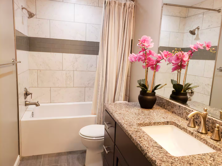 Bright bathroom with soaking tub, marble tile surround, granite countertop vanity and pink orchid arrangement