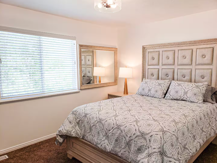 Bright bedroom with tall tufted panel headboard, neutral bedding, large mirror and warm bedside lamps