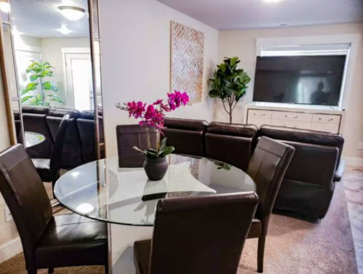 Open dining area with glass table, leather chairs and orchid centerpiece
