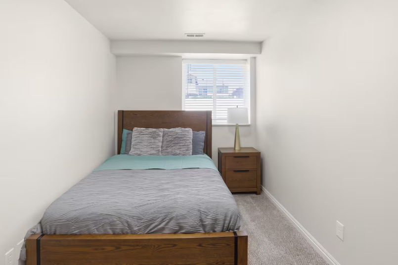 Lower level queen bedroom with dark wood platform bed, teal bedding, plantation shutters and nightstand lamp