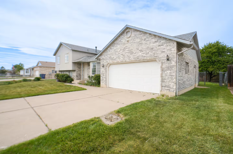 Side view of brick and stucco home with 2-car garage, wide concrete driveway and lush green lawn