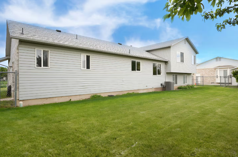 Rear exterior of home showing two-story siding, multiple windows, AC unit and expansive green lawn