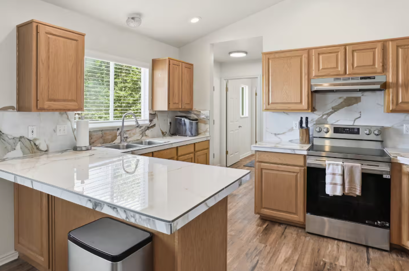 Kitchen with oak cabinets, marble backsplash, center island with marble countertop, stainless steel range and hardwood floors